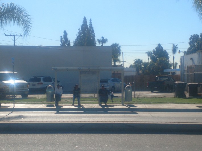 Riders sit at a newly installed bus shelter on the southeast corner of McFadden Avenue, near Main Street. While the bus stop provided a sitting area where there previously was not, the roof didn't provide shade coverage for sitting bus patrons. Kristopher Fortin/Streetsblog CA