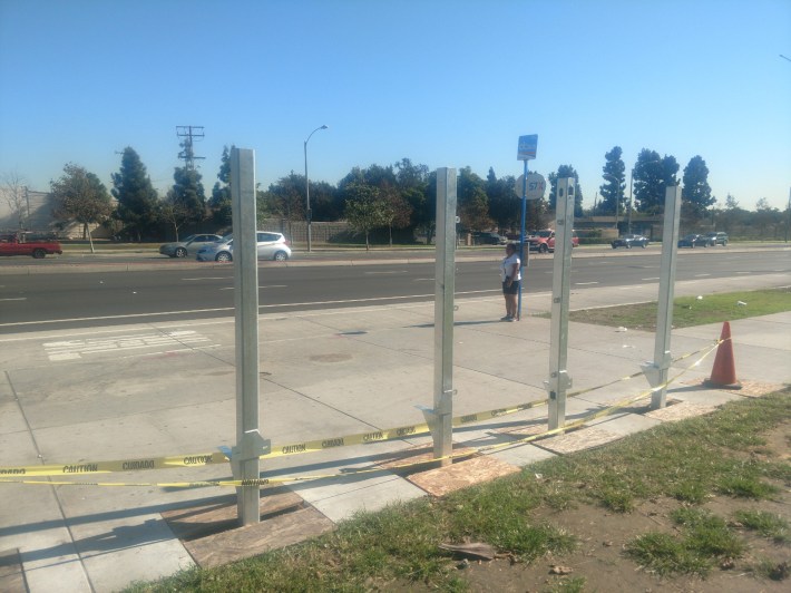 A bus rider takes shelter under a bus stop sign at the corner of Bristol and First Streets. with the base of the new bus shelters still being installed. Kristopher Fortin