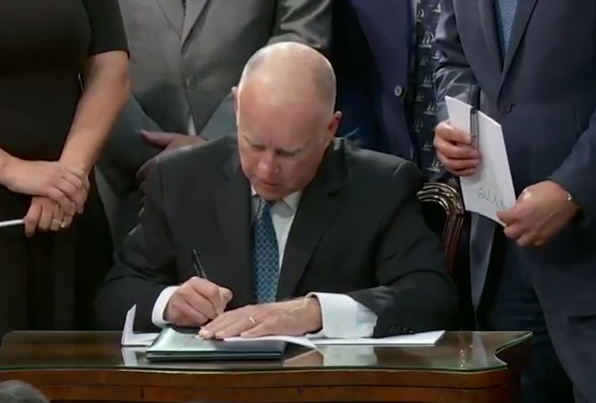 Governor Brown jokes as he signs several copies of the bill. Image: Screengrab CA Senate