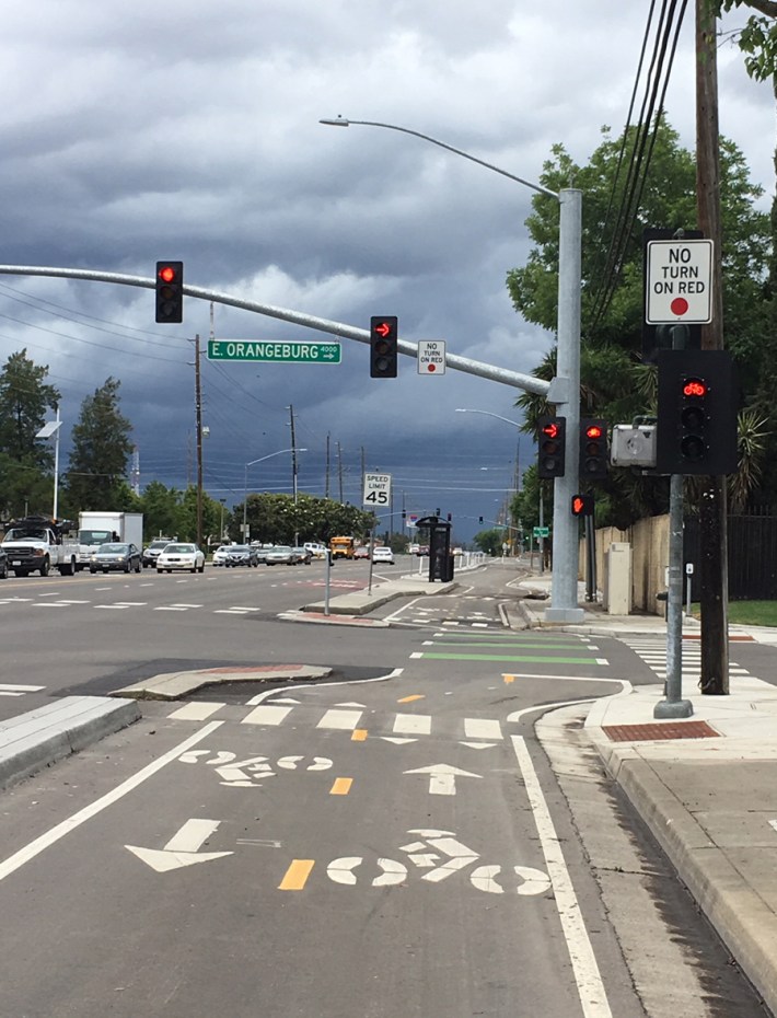 This new two-way cycle track includes cement curb protection, a raised bus stop island, and bike signal heads at an intersection with "no right turn on red" indicators.