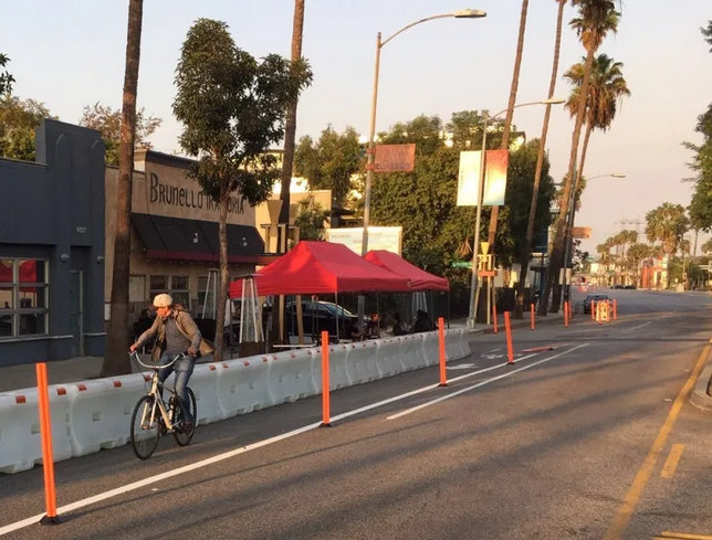 Bicyclist rides in lane protected by temporary posts, outside street dining area