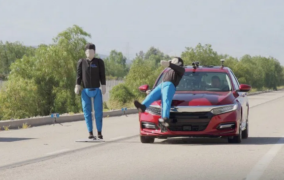 two fake pedestrians, one on side of busy road, one in road being hit by car