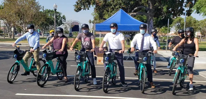 A row of cyclists on bike-share bikes, wearing masks