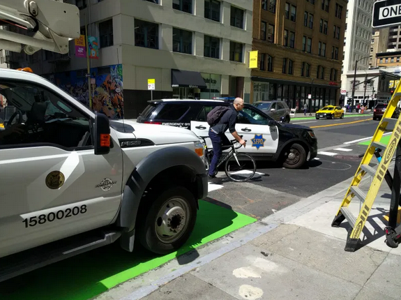Police vehicle blocks bike lane; another police vehicle turns into a bicyclist trying to get around it