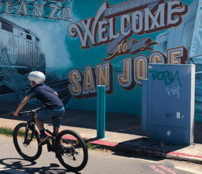 Boy rides bike past mural in San Jose