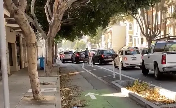 bike rider forced to squeeze between cars
