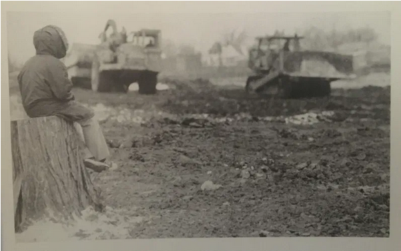 Black and white photo of a young man looking at bulldozers clearing land
