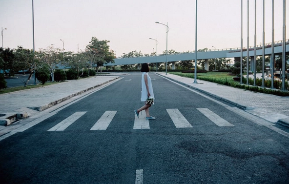 A woman in a white dresses crosses a street in the crosswalk