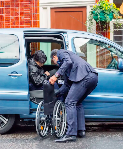 A man folds a wheelchair next to a woman sitting in a van