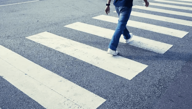 person seen from the legs down walks on crosswalk striping