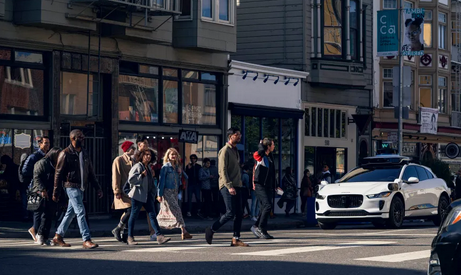people cross a street in front of a waiting autonomous vehicle