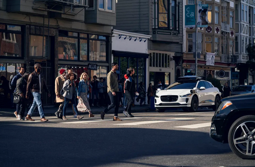people cross a street in front of a waiting autonomous vehicle